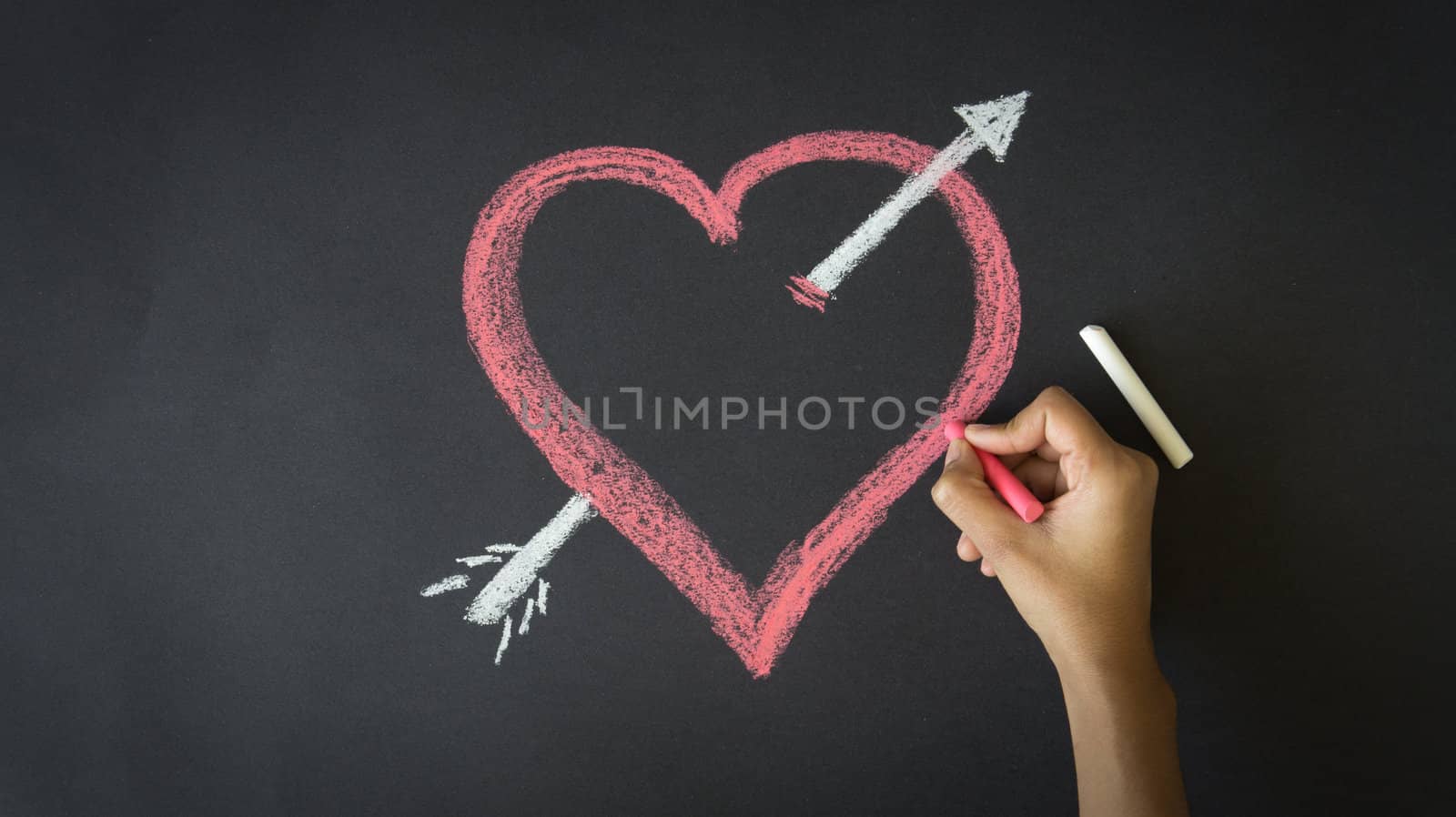 Person drawing a Valentines Day Heart with chalk on a blackboard.