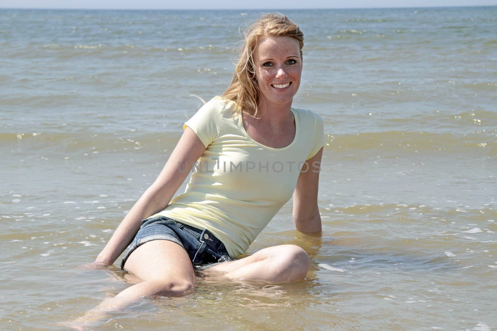 Beautiful happy woman sitting in the water from the ocean