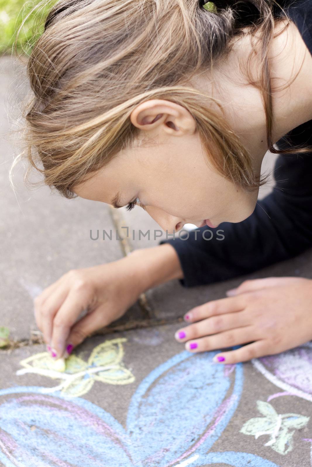 Girl drawing with chalk on pavement by annems