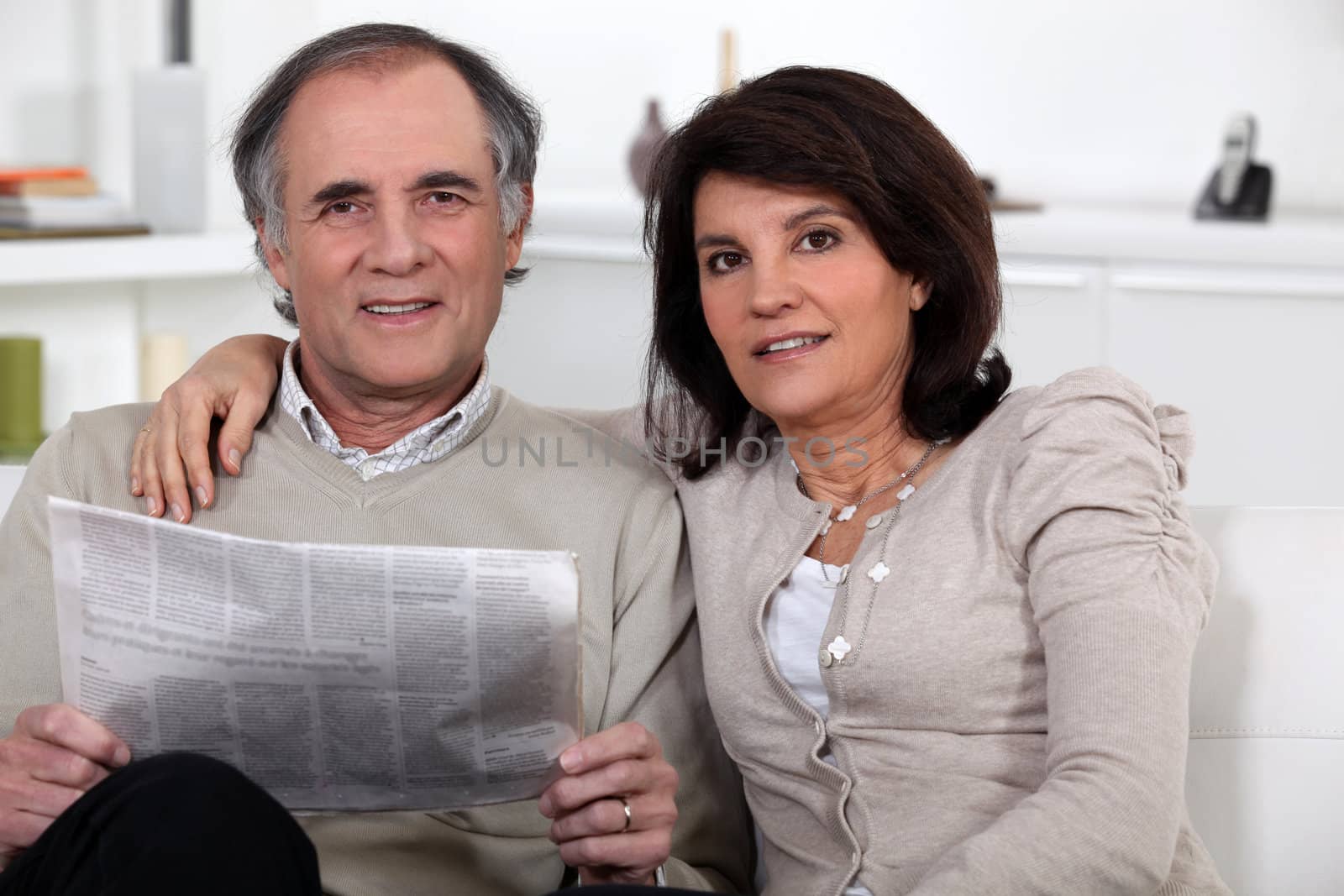 Couple sitting reading a newspaper by phovoir