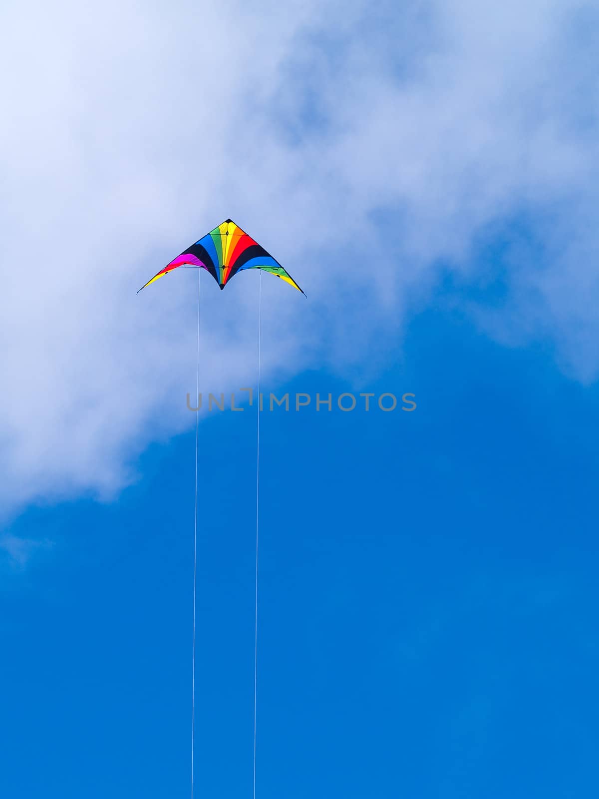 A rainbow colored stunt kite against a blue sky with wispy clouds.