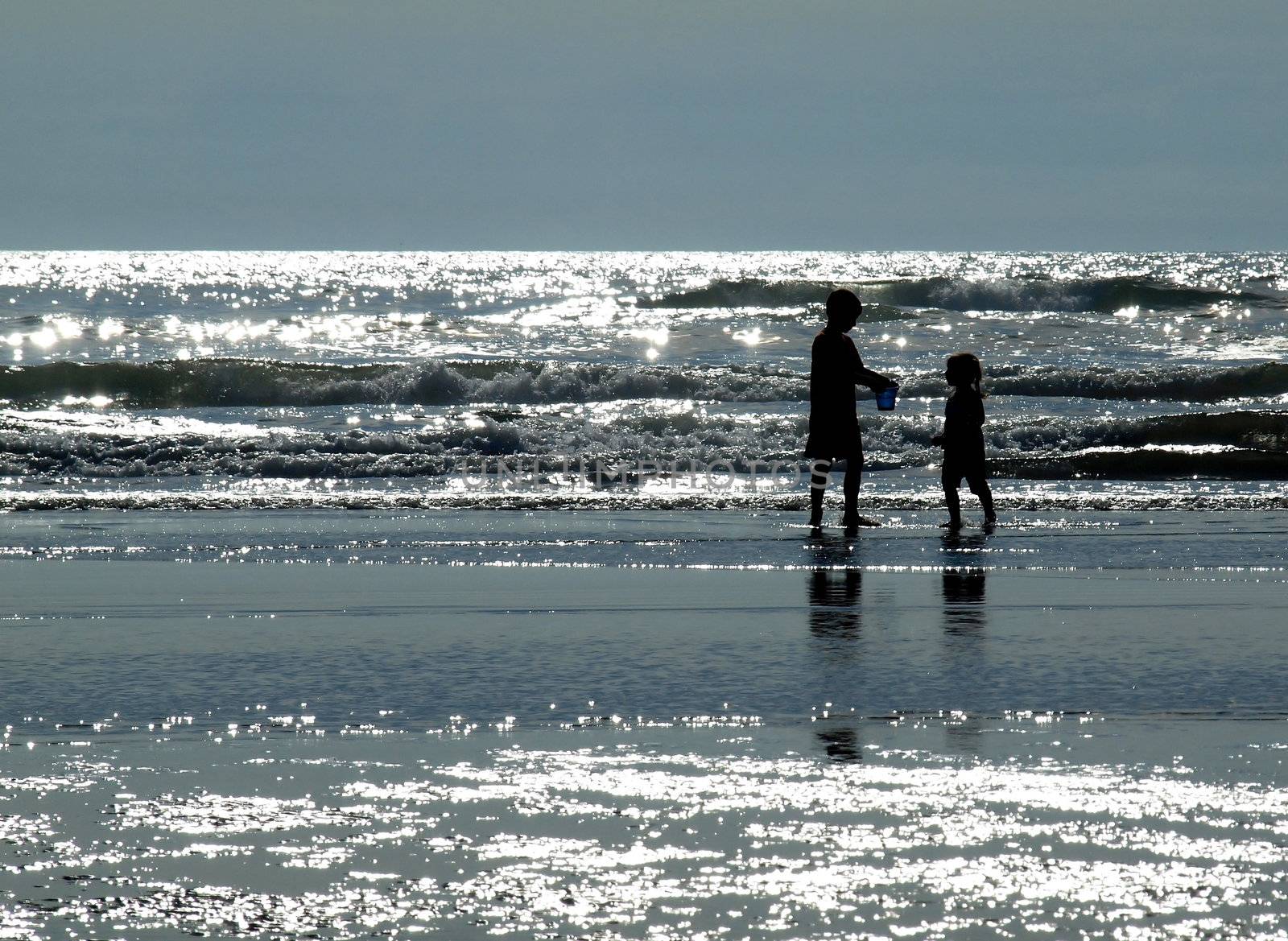 Two Kids Playing on the Beach as the Sun is Glistening on the Water