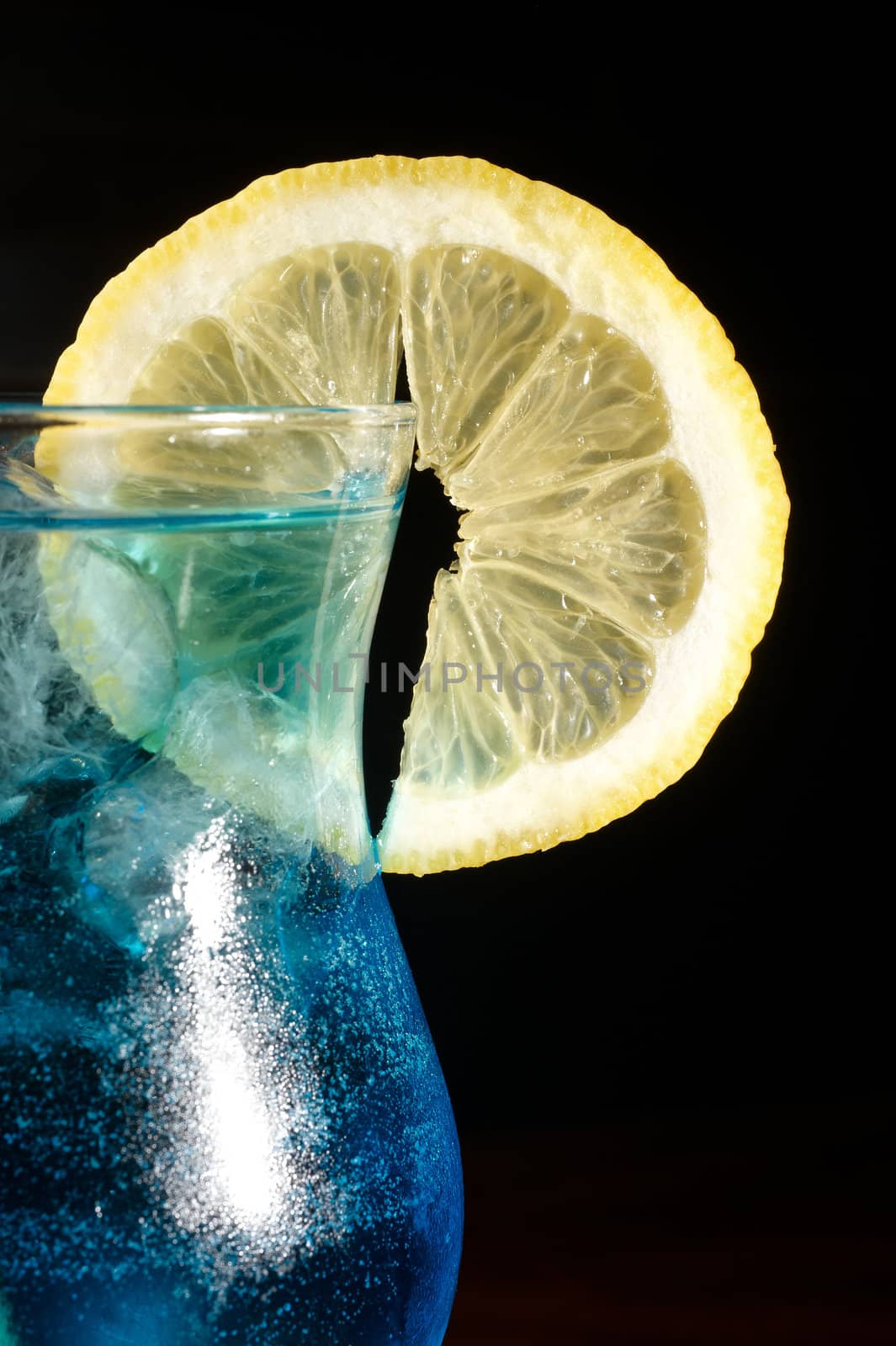 close-up of blue curacao cocktail with slice of lemon on a black background