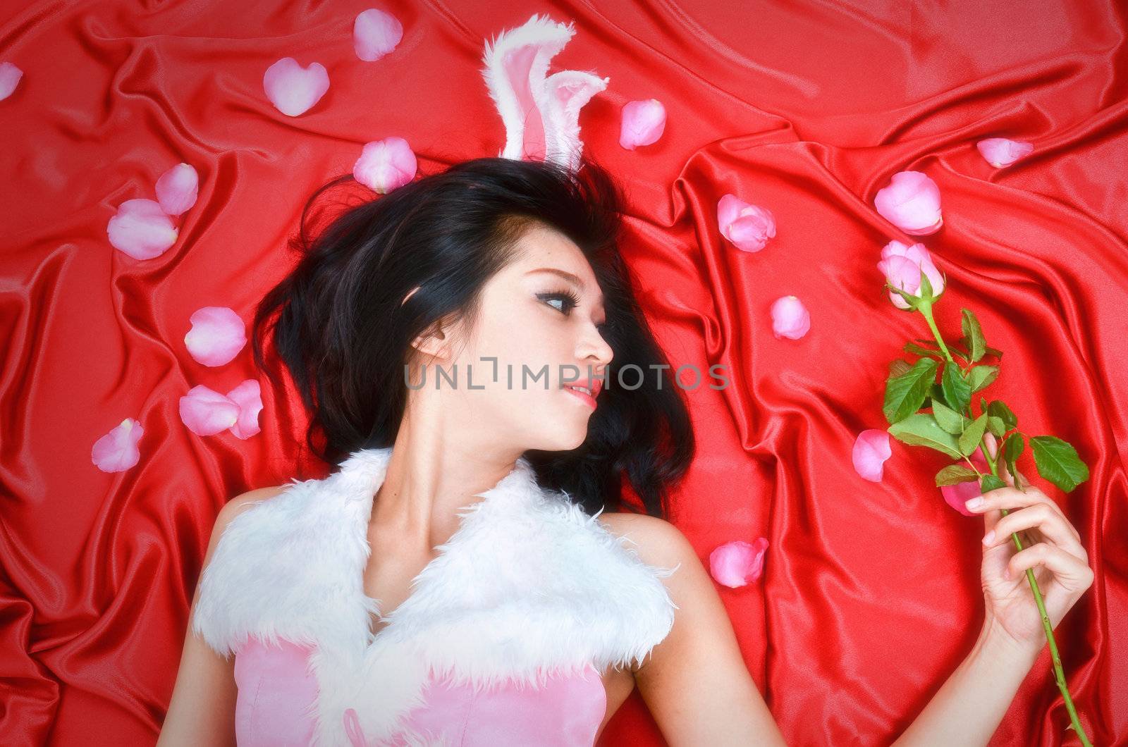 Sexy bunny girl hold pink rose lie on red fabric
