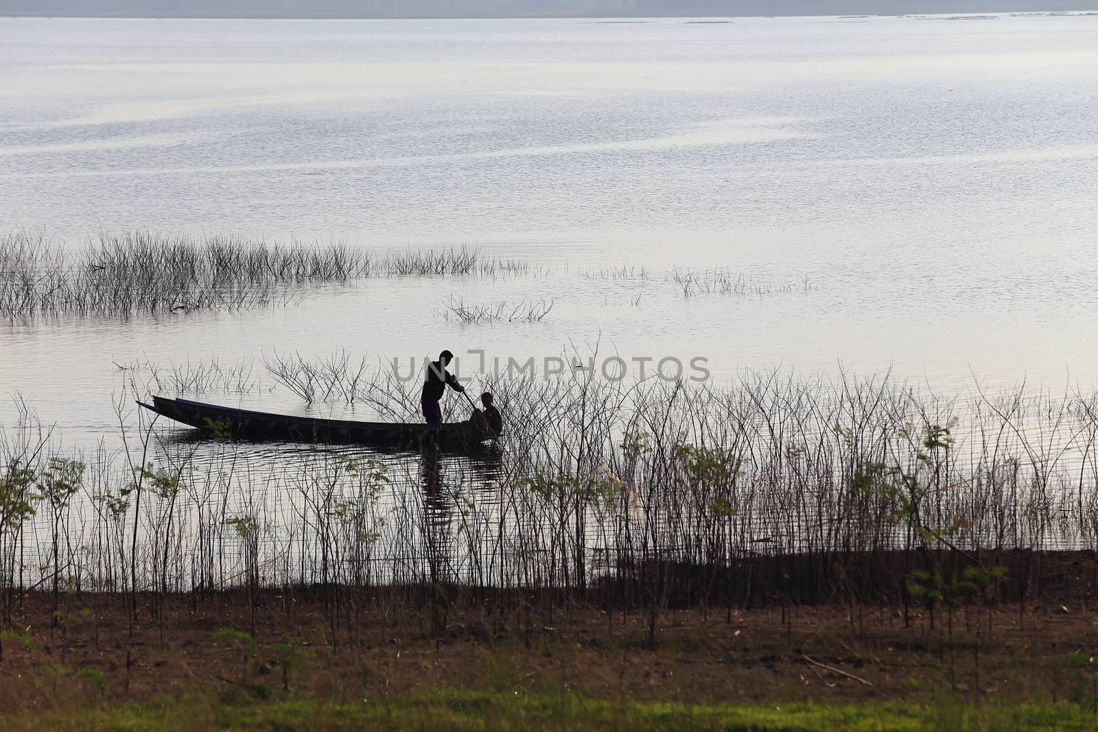 silhouette of fisherman on wood boat at lake.