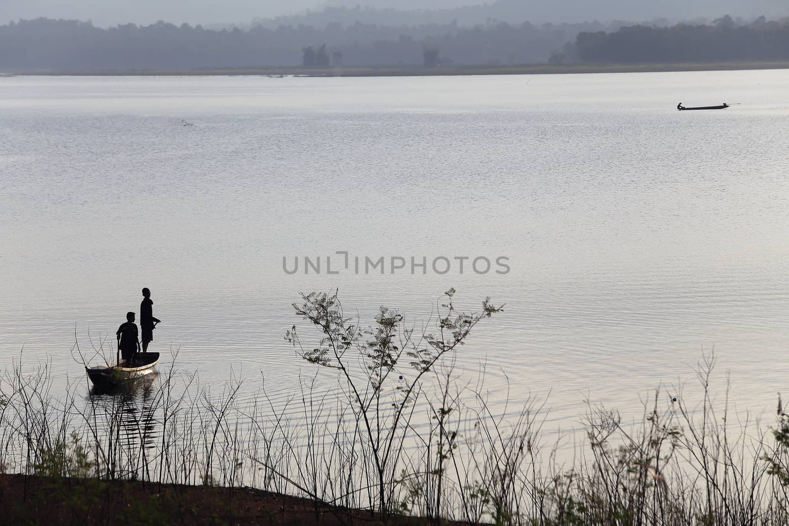 silhouette of fisherman on wood boat at lake.