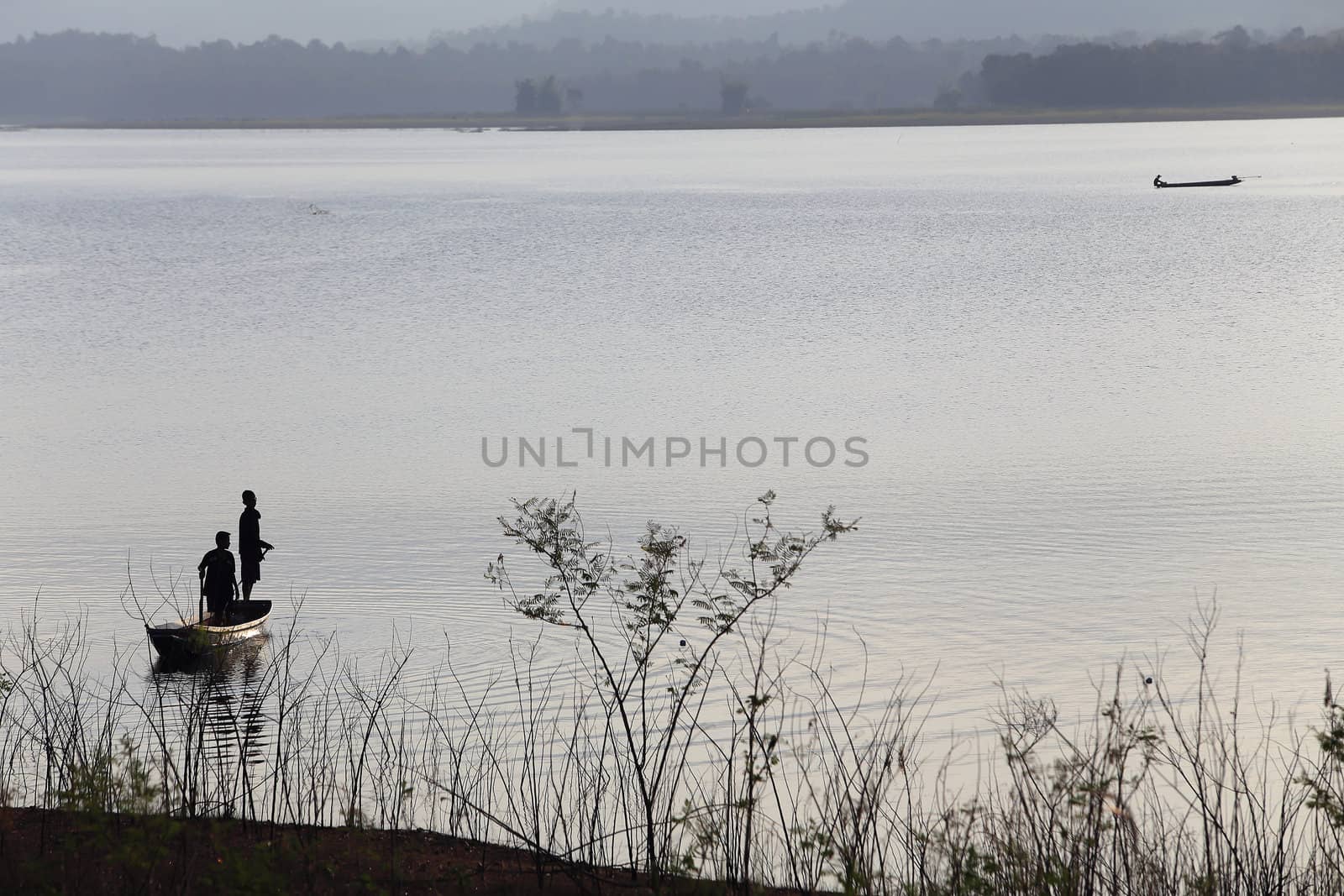 silhouette of fisherman on wood boat at lake. by rufous