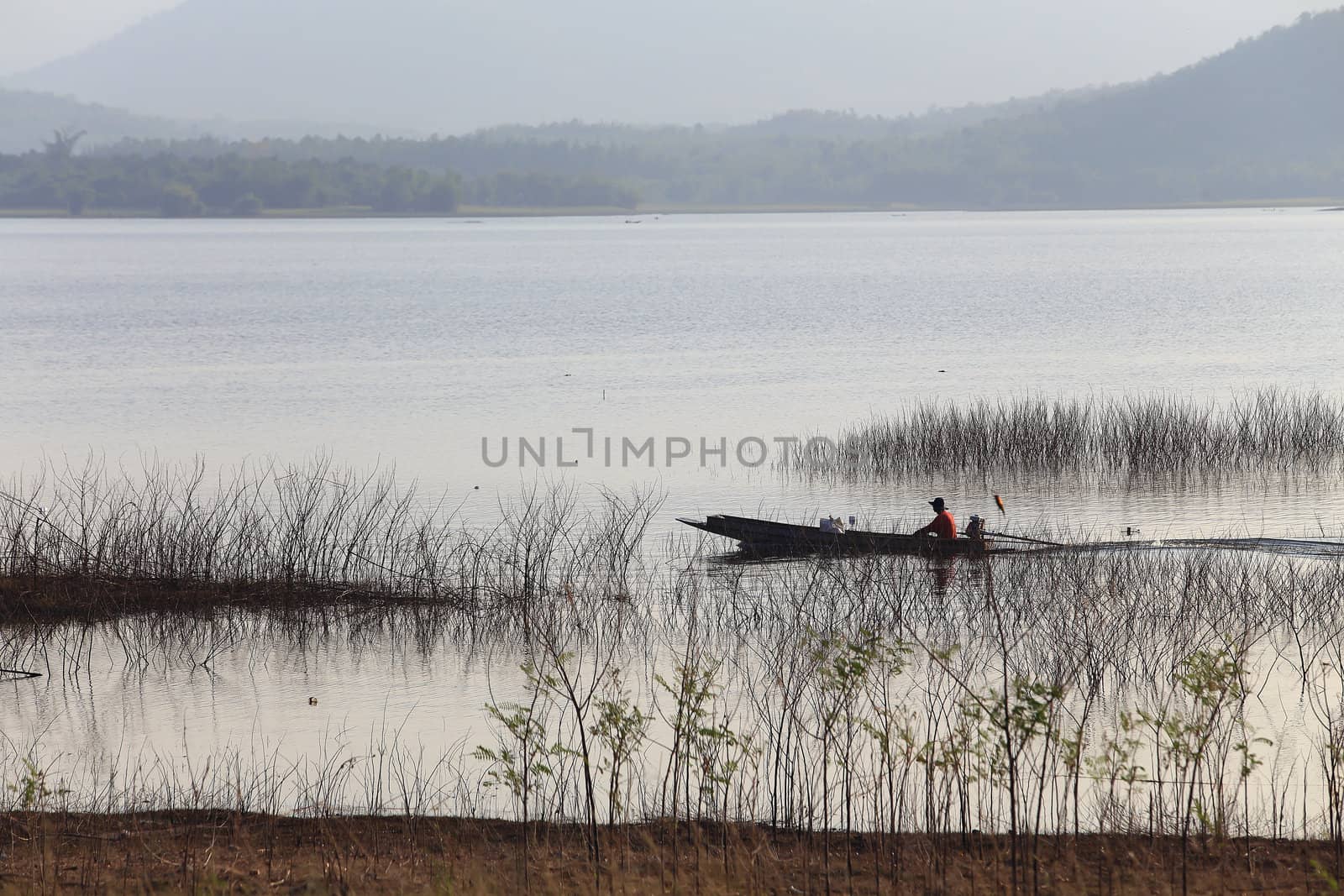 silhouette of fisherman on wood boat at lake. by rufous