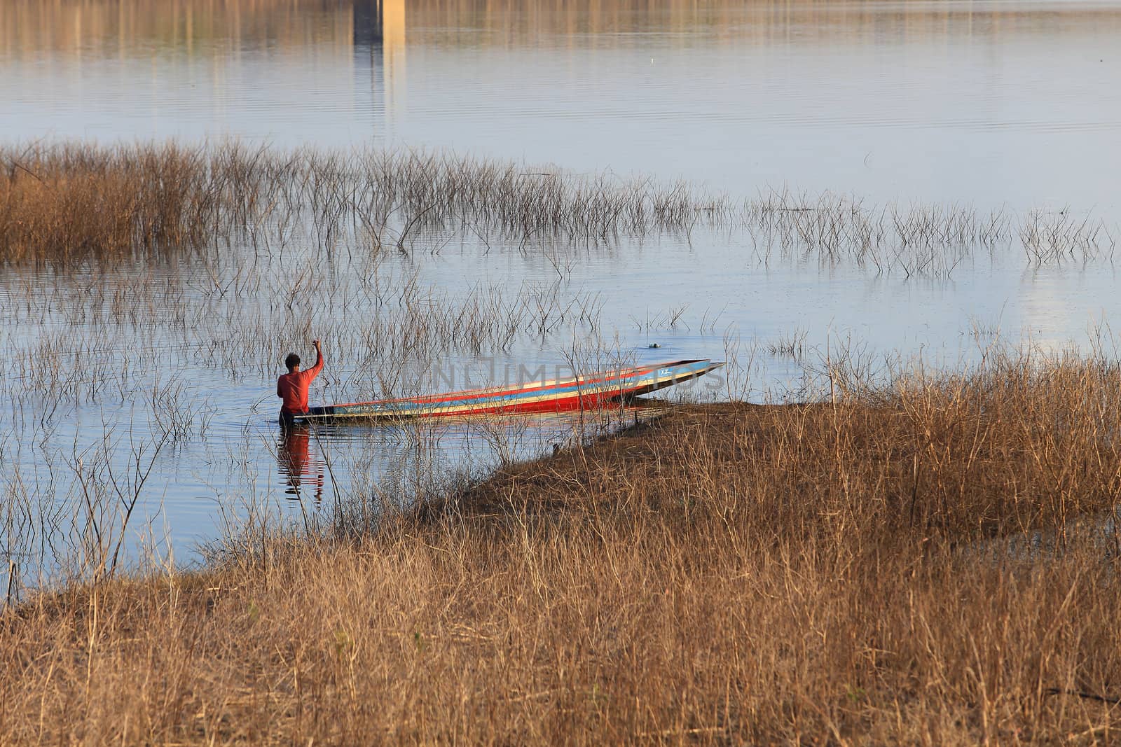 silhouette of fisherman on wood boat at lake. by rufous