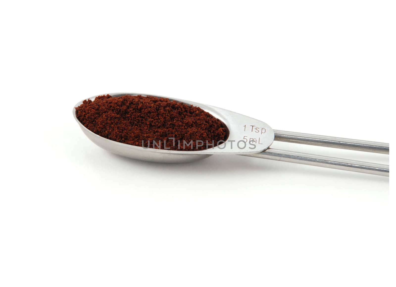 Ground cloves measured in a metal teaspoon, isolated on a white background