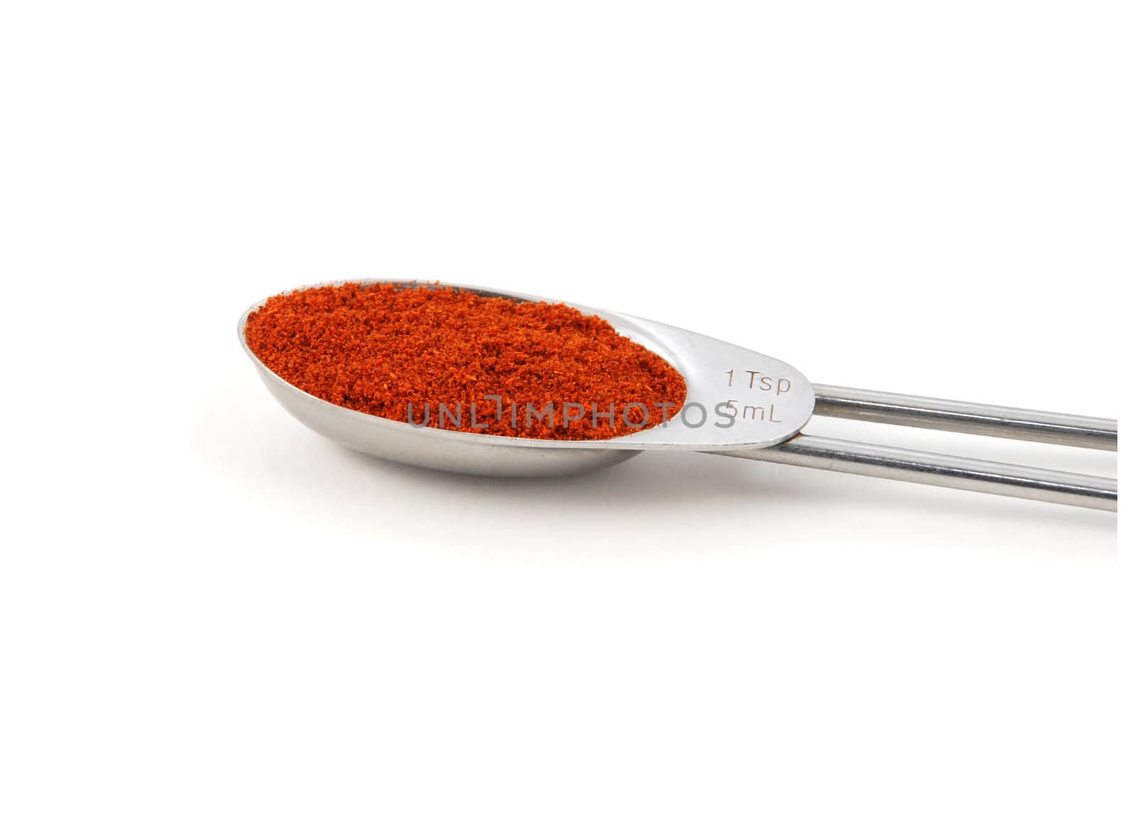 Chilli powder measured in a metal teaspoon, isolated on a white background