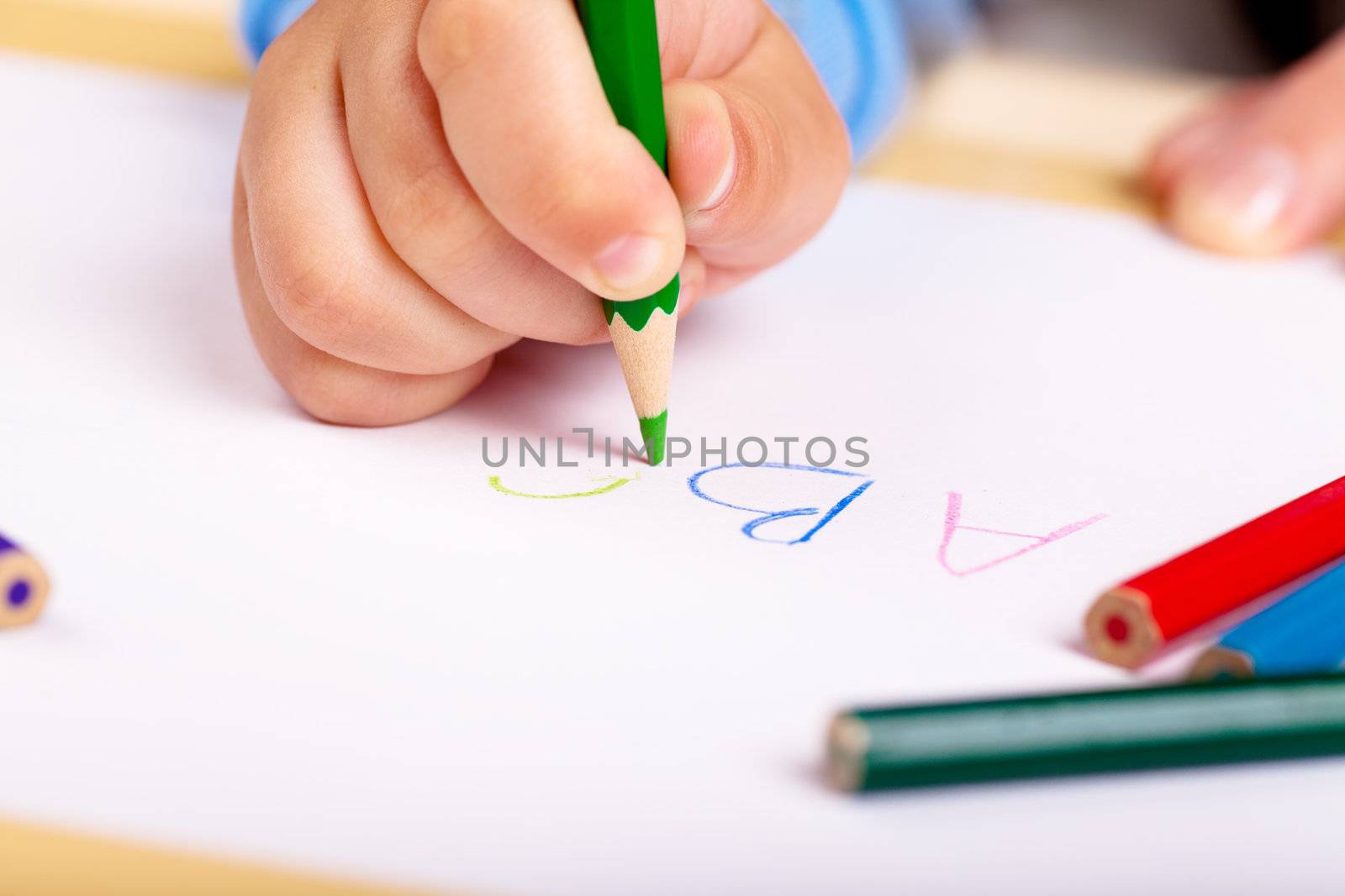 Child's hand drawing letters with green pencil