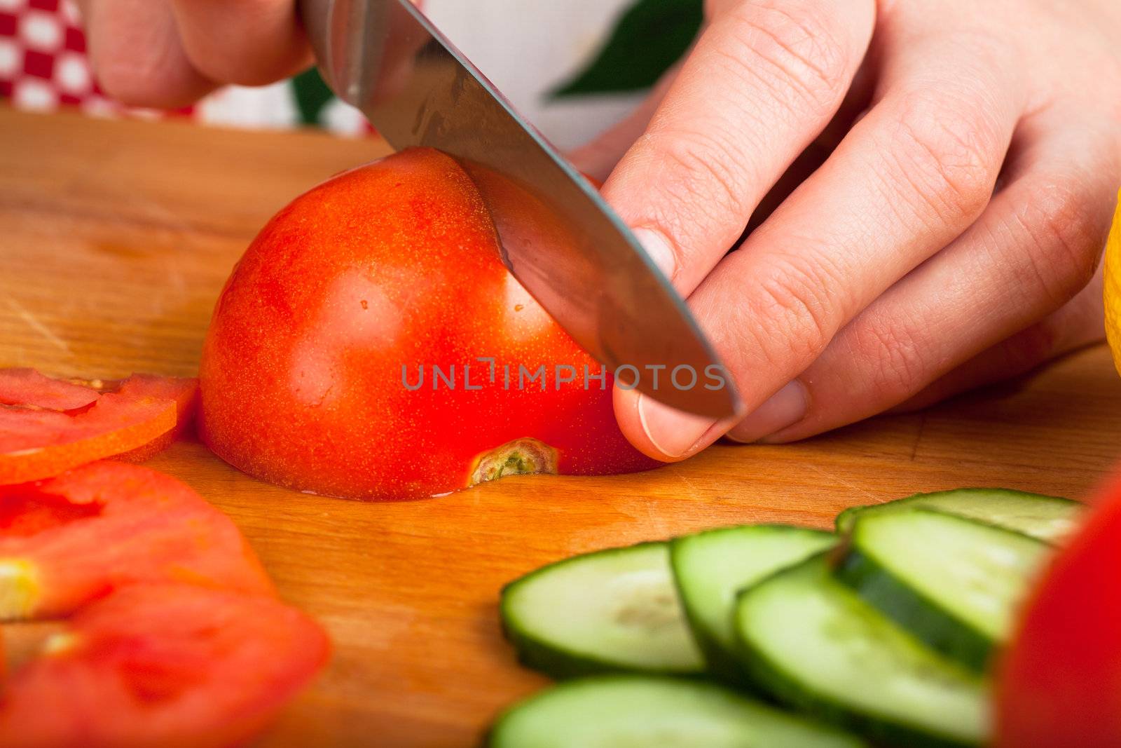 Woman cutting vegetables (tomato, cucumber, salad) on a wooden table
