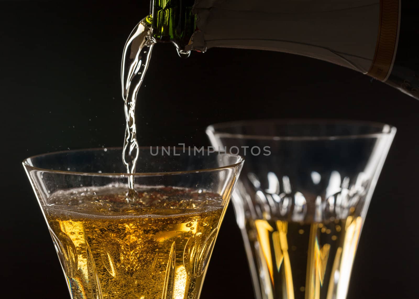 Detail of a pair of cut glass champagne goblet with a heart on the side and drink being poured