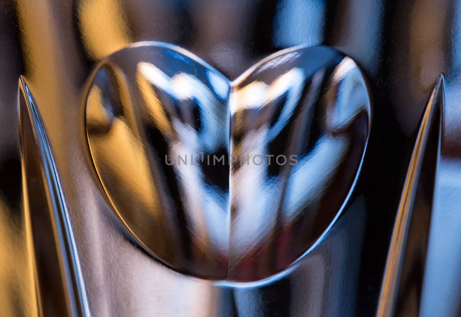 Detail of a cut glass champagne goblet with a heart on the side and reflecting lights from background