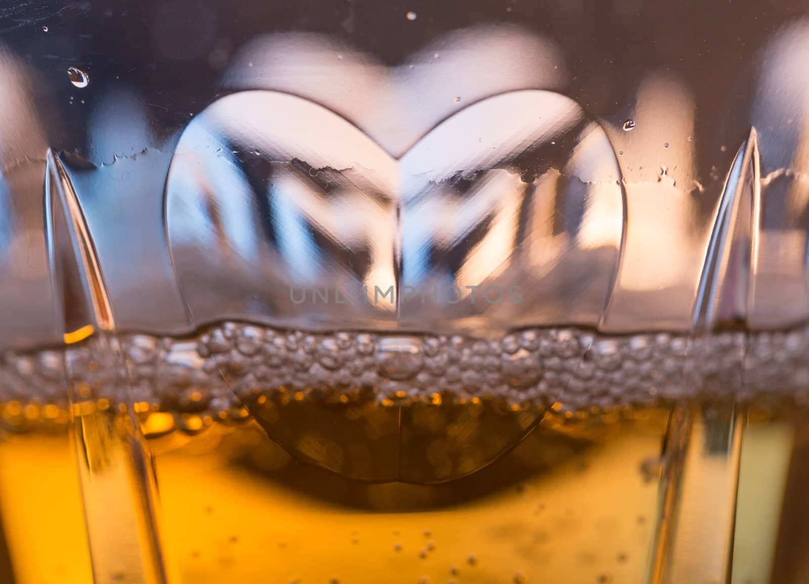 Detail of a cut glass champagne goblet with a heart on the side and drink being poured