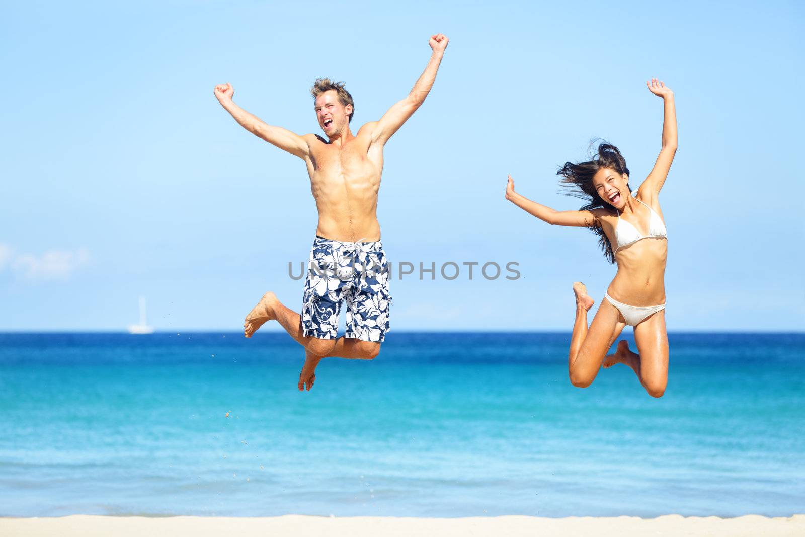 Beach people - happy couple jumping in swimwear and bikini. Sunny summer travel image with young multiethnic couple on Hawaii, Big Island. Caucasian man, Asian woman