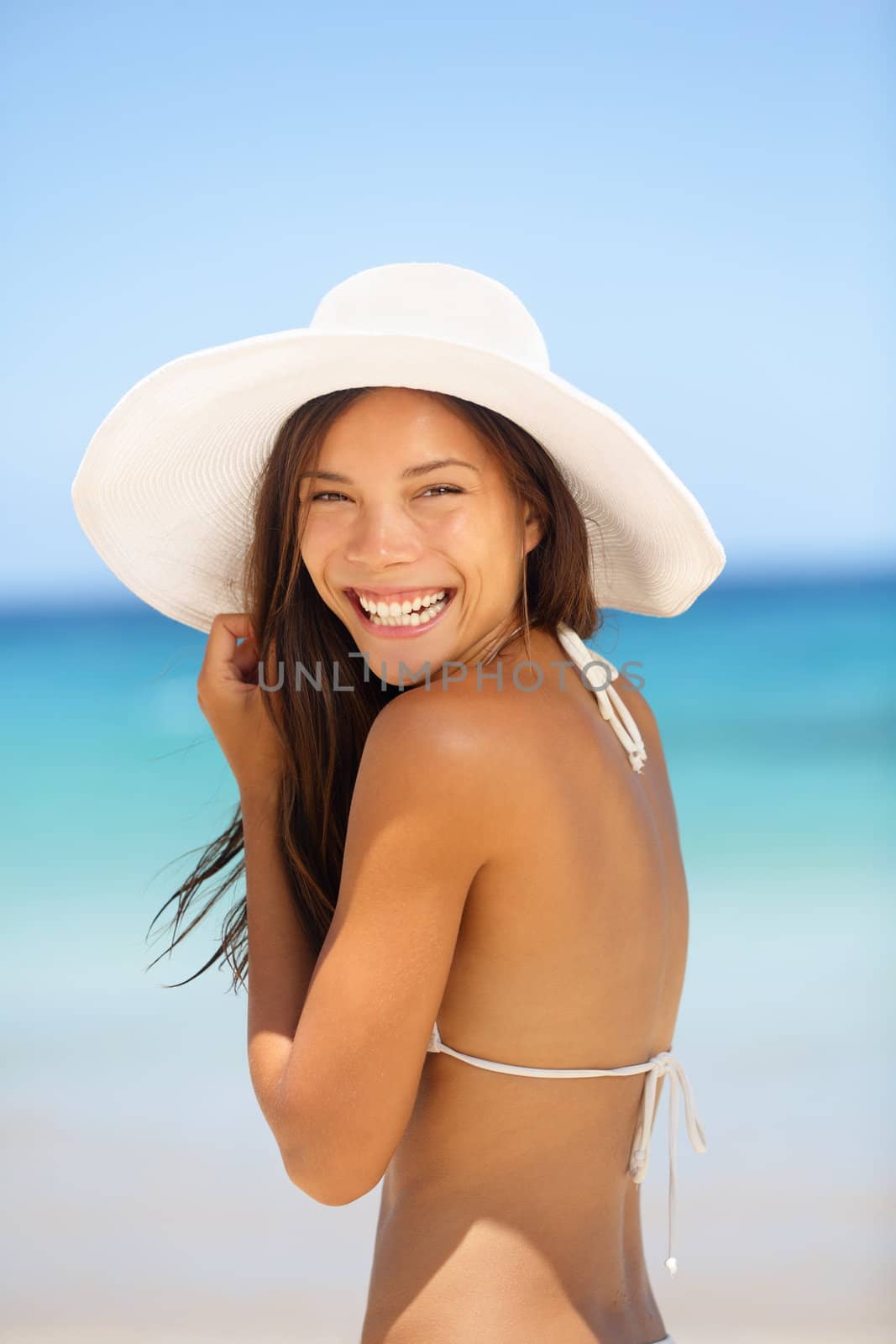 Asian woman beach portrait. Happy lifestyle photo of mixed race Asian Chinese / Caucasian young lady in bikini smiling pretty wearing beach hat on summer holiday vacation.