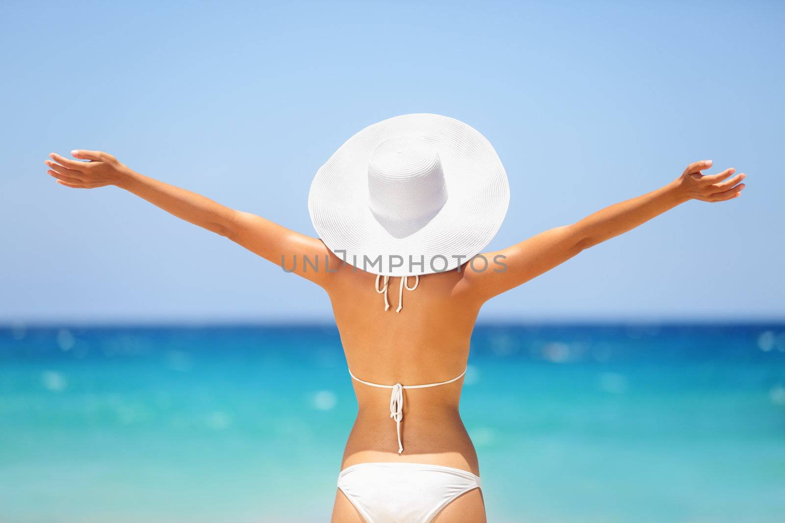 Beach summer holidays woman in happy freedom concept with arms raised out in happiness. Woman model wearing white bikini and beach hat on Big Island, Hawaii.