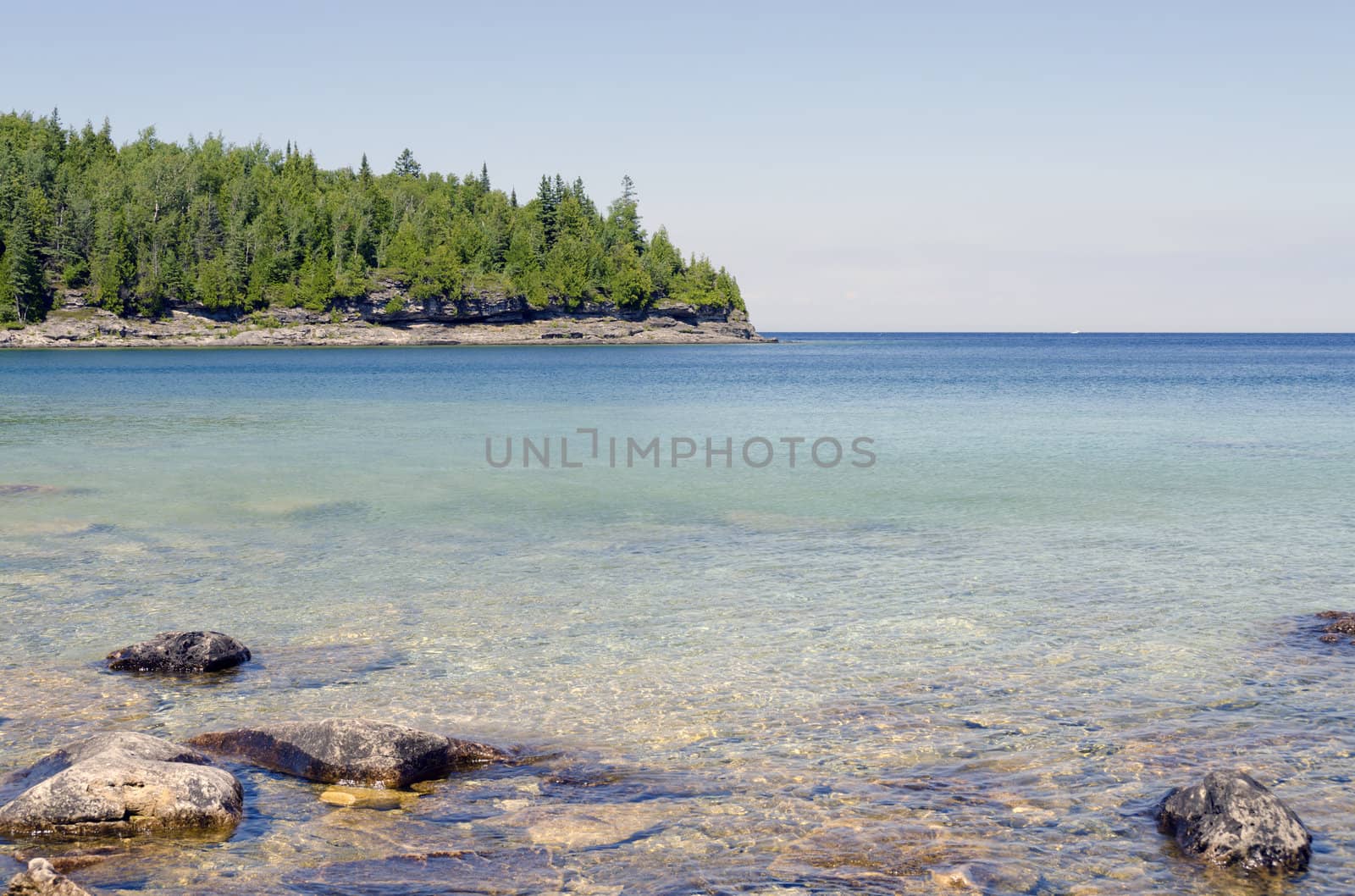 Green and blue water of Huron Lake, Ontario under blue sky.