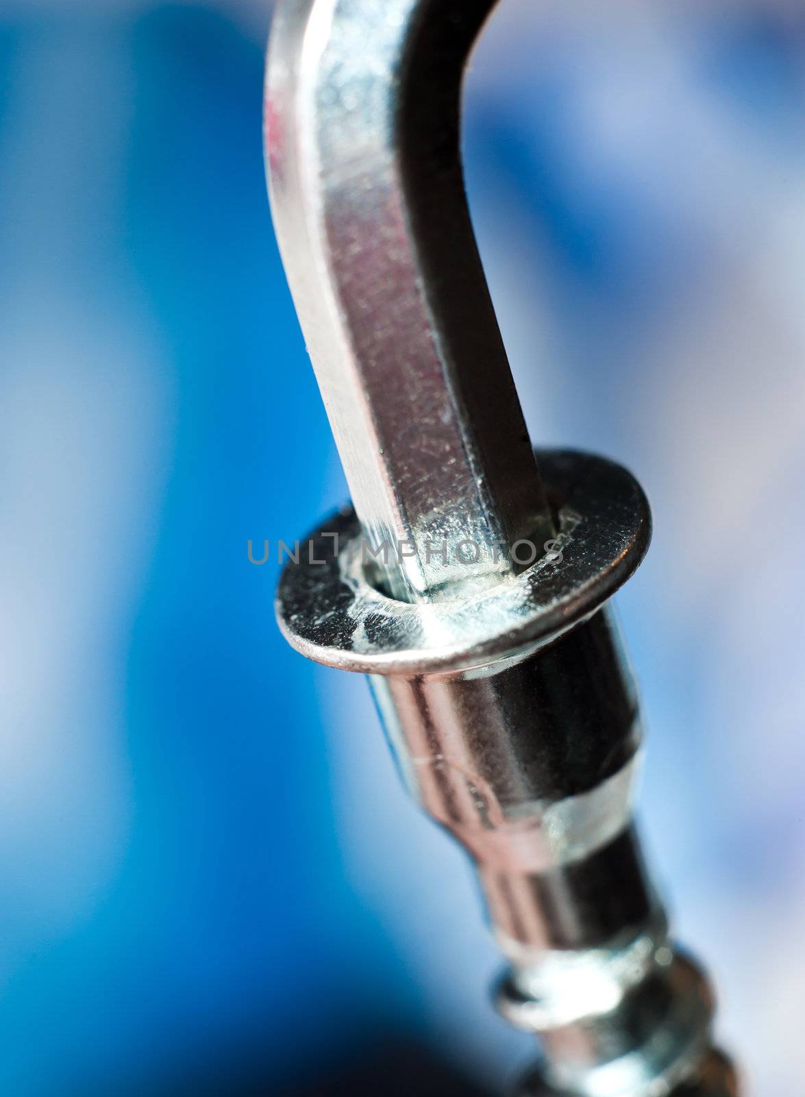 A chrome cap head or allen screw with a wrench on blur background