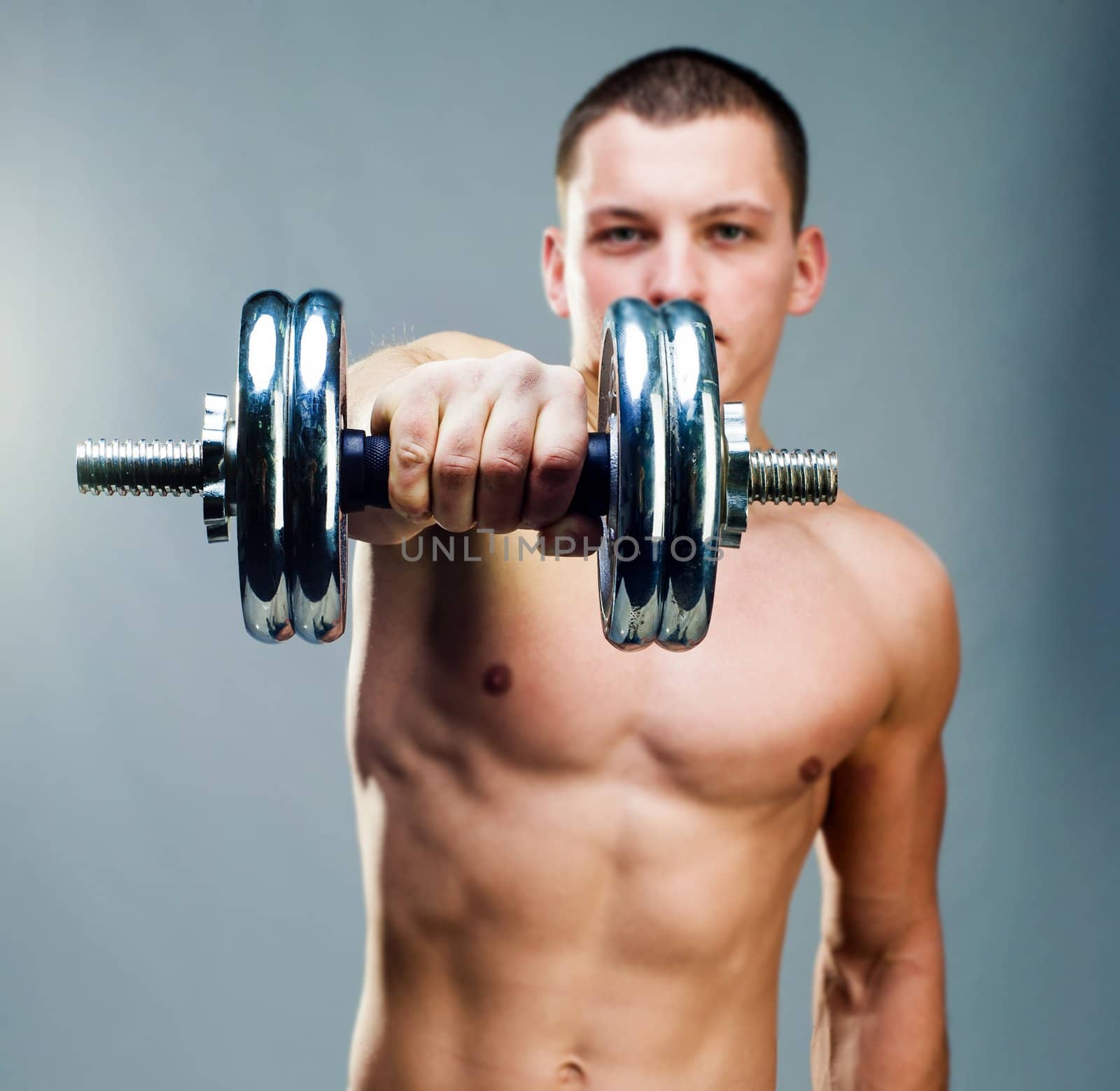 handsome man holding a dumbbell in front on a gray background