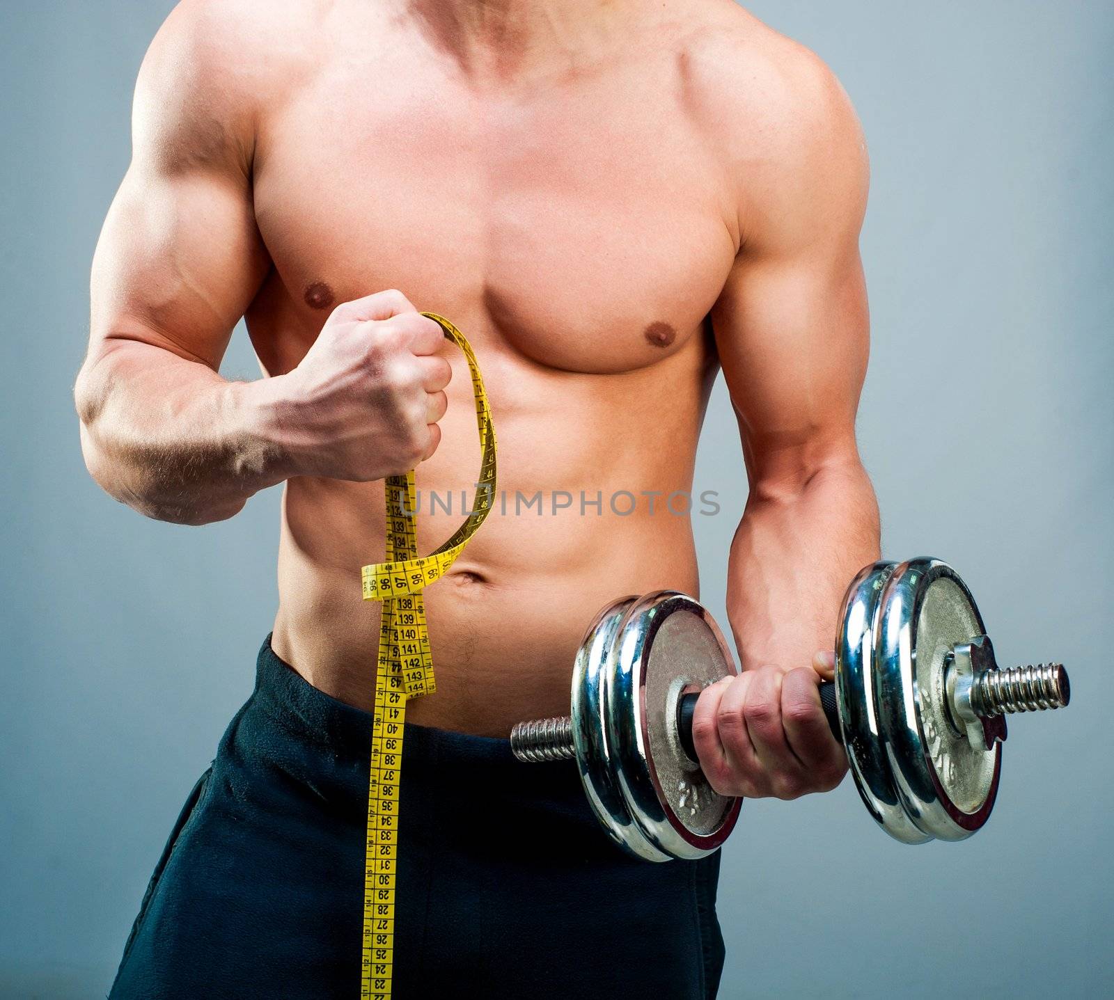 muscular man measuring his biceps with dumbbells