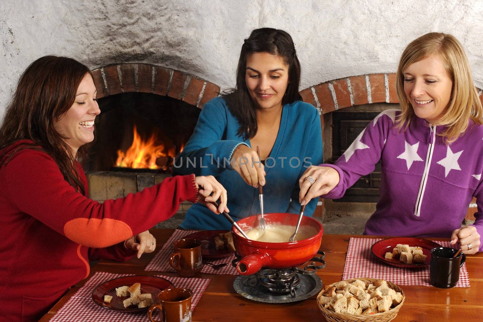 Photo of three beautiful females dipping bread into the melted cheese in a fondue pot.