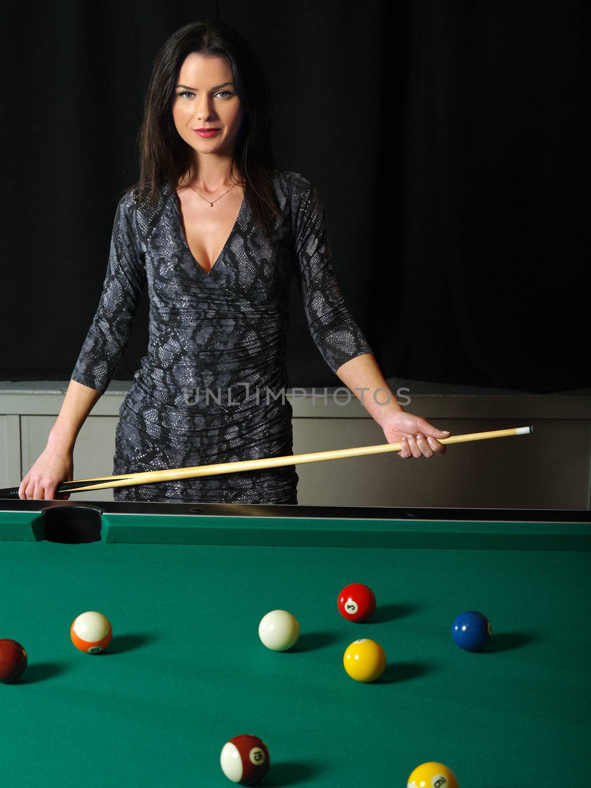 Photo of a beautiful brunette holding a pool cue and playing pool.
