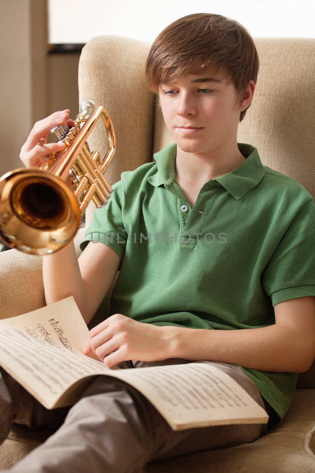 Photo of a teenage male reading sheet music and practicing his trumpet at home.
