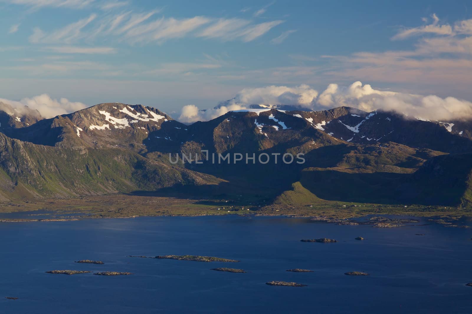 Scenic mountain peaks on Lofoten islands in Norway covered in scattered clouds with small fishing villages on the coast and rocky islands in the sea