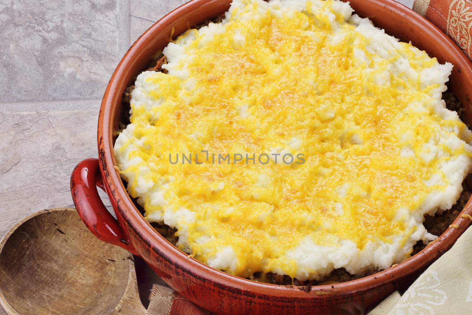 Shepard's Pie in a rustic casserole dish with wooden spoon. 
