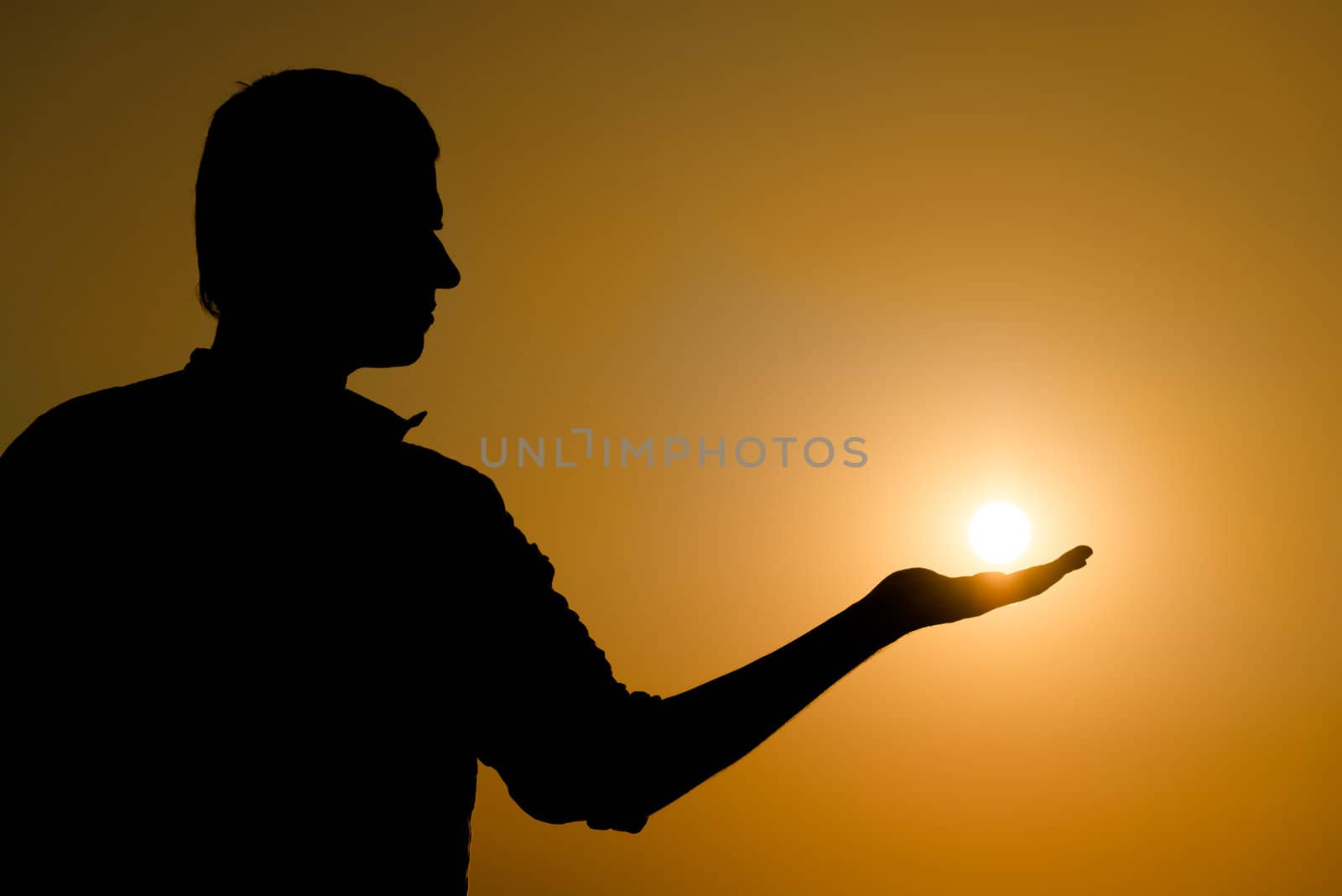 Silhouette of young man holding the sun on his hand at yellow sunset background