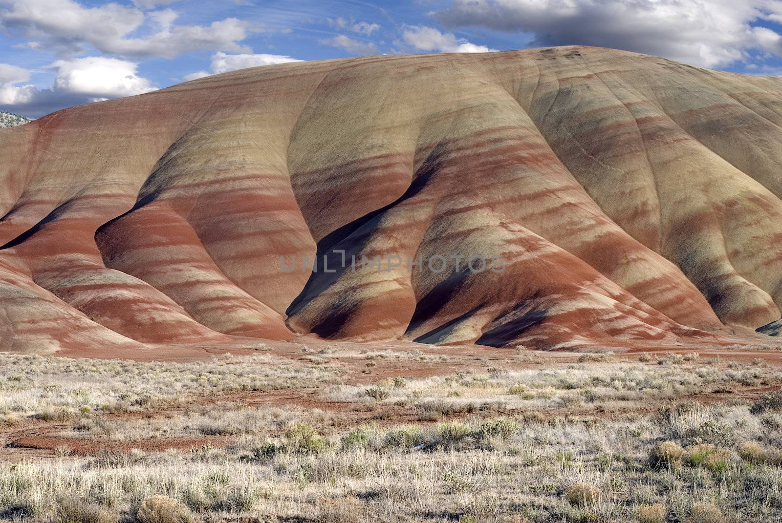 Horizontal landscape of the colorful Painted Hills in Oregon aganist cloudy blue skies.