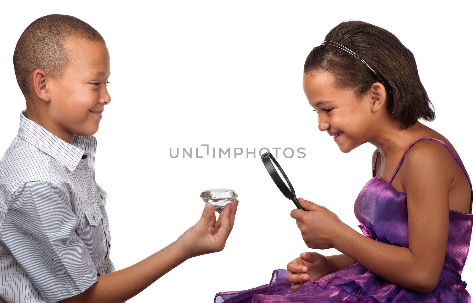 A young boy offers a large diamond to a young girl, who inspects it with a magnifying glass.