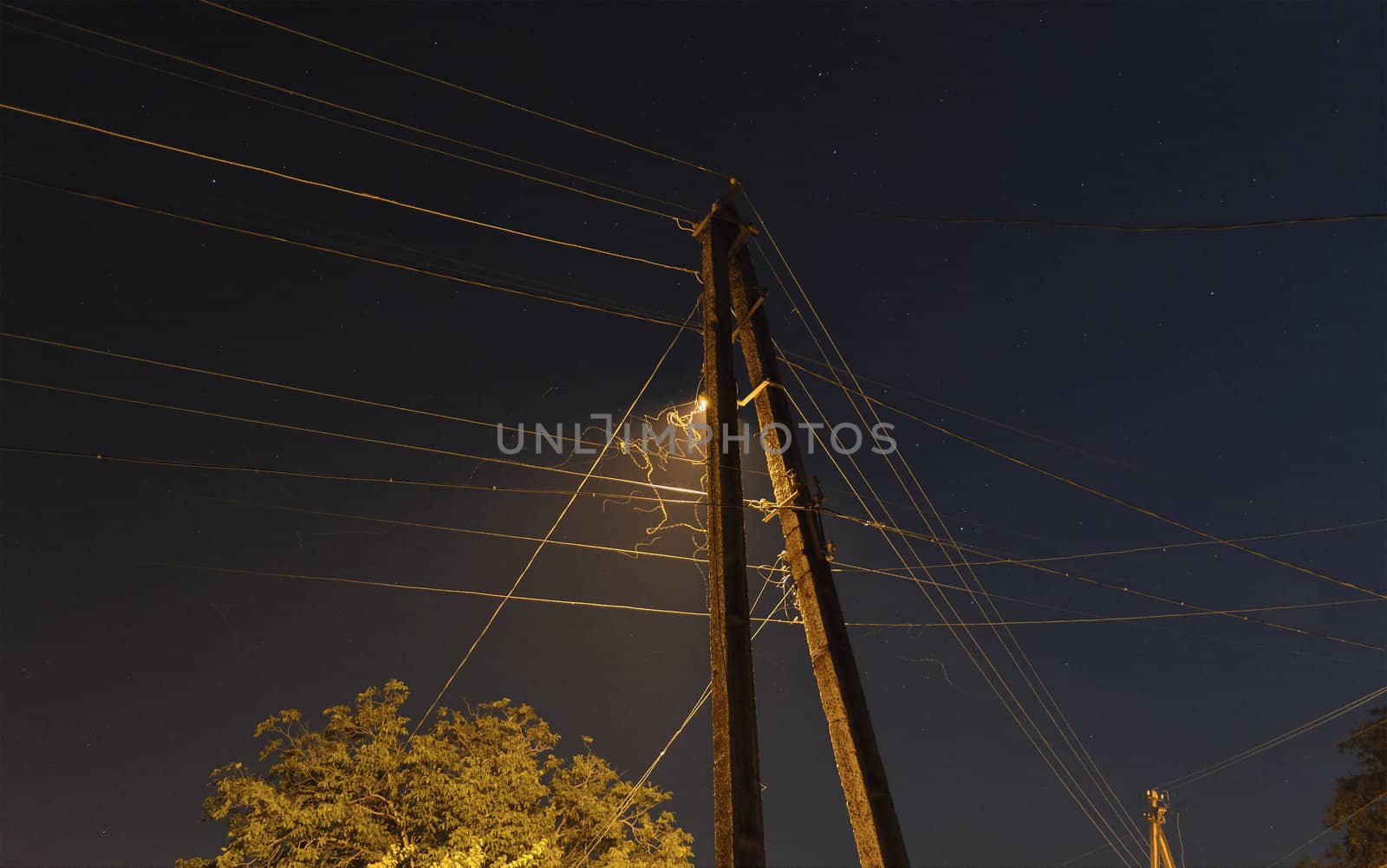 Image power pole with electrical wires, with street lamp and flight paths of moths at night.