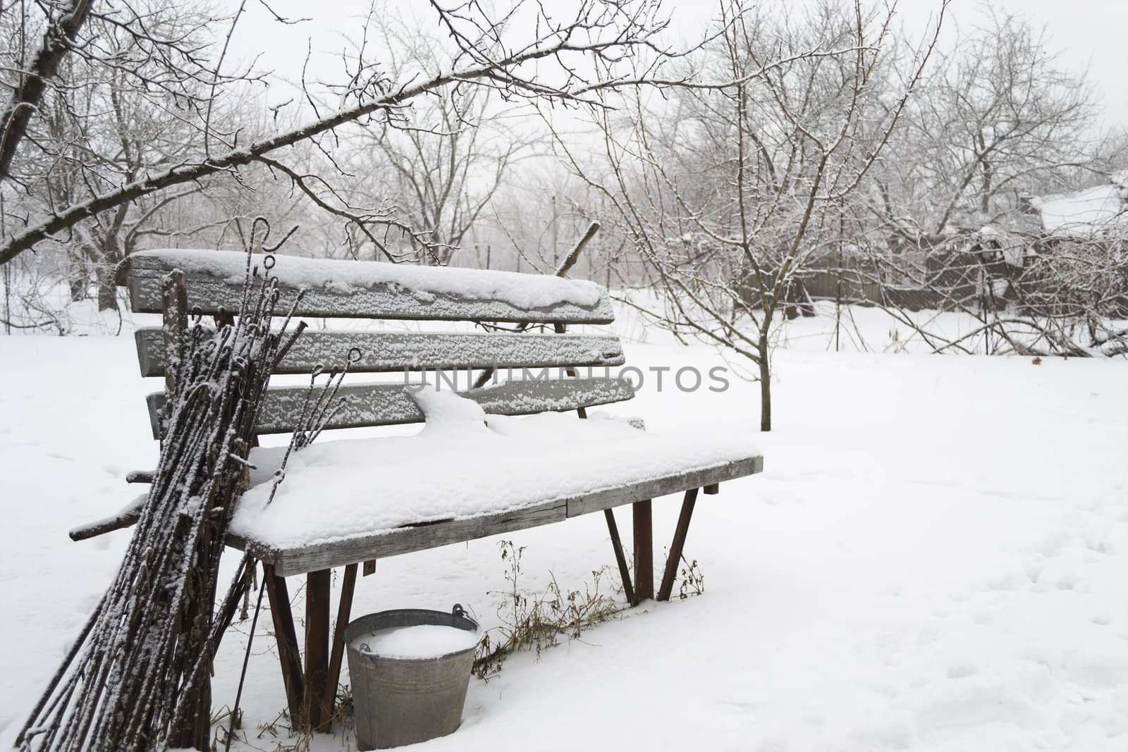 Snow-covered bench with forgotten garden tools in the winter garden.