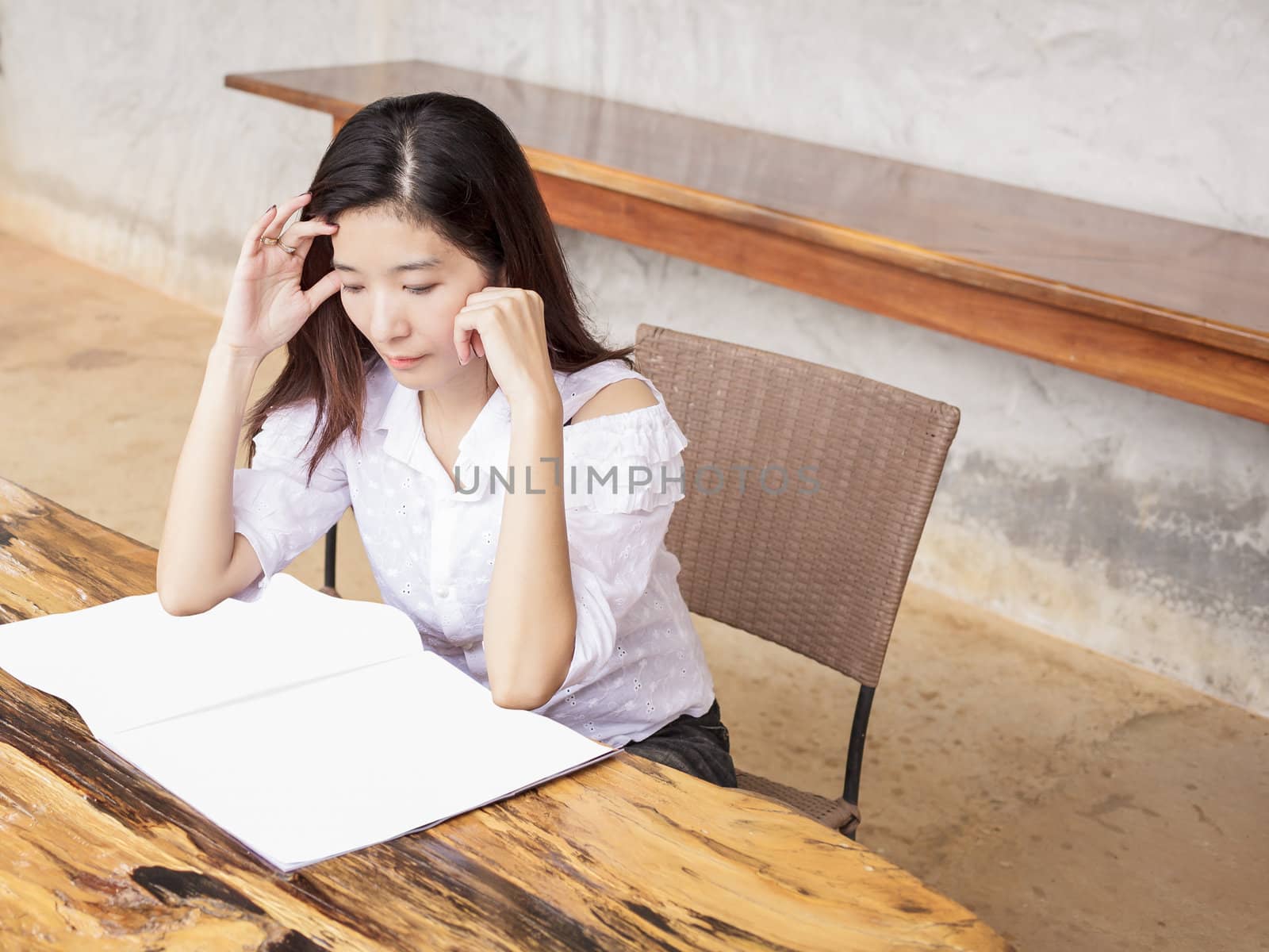 young woman reading book or magazine on wood table by FrameAngel