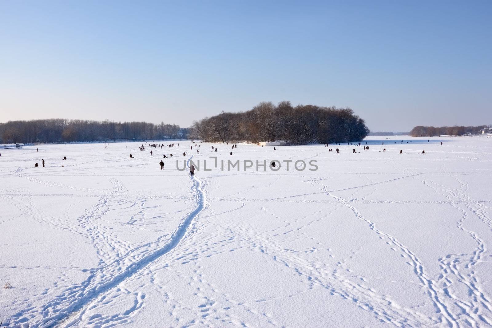 Winter scene. Fishermans catch fish in river on the ice surface with snow