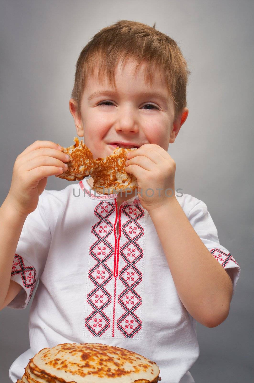 Russian little boy eats pancakes with red caviar.