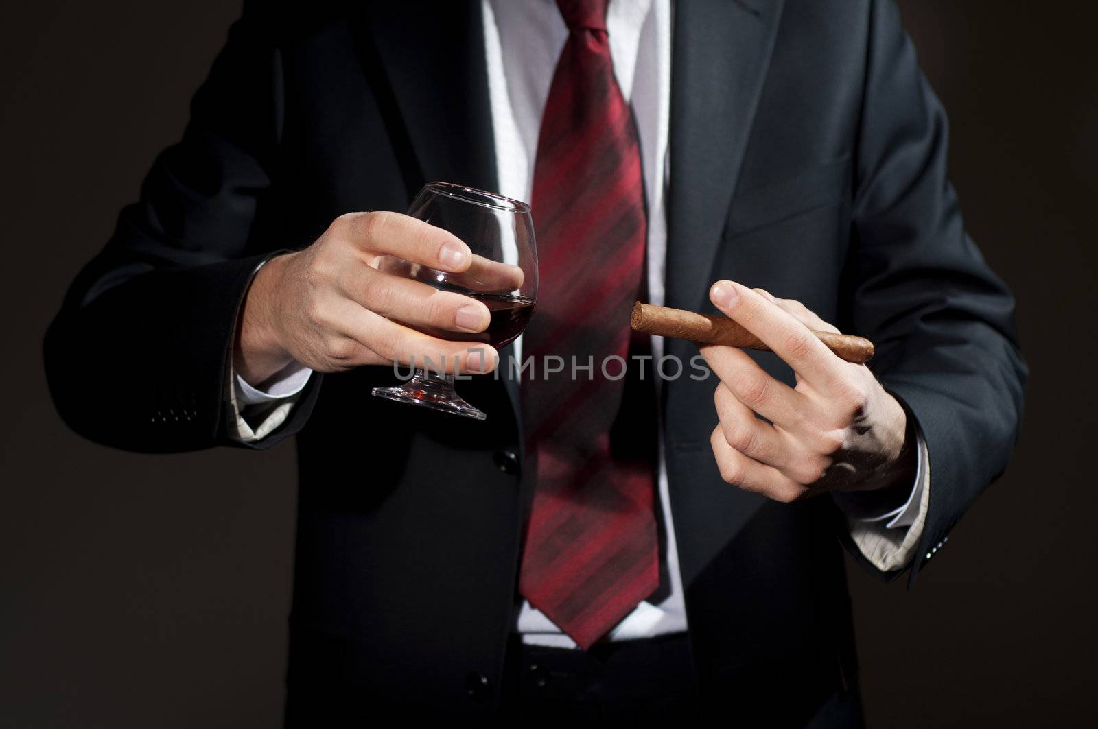 man in a business suit holds a cigar and a glass with whisky