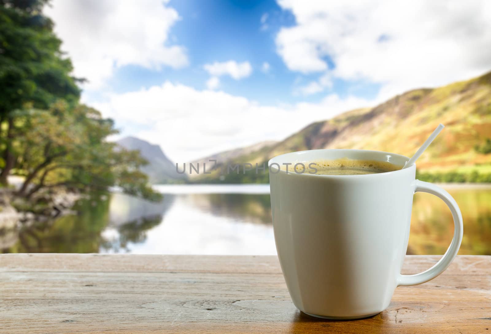 Coffee in white pottery cup on old wooden table with blurred image of lake district in England as background