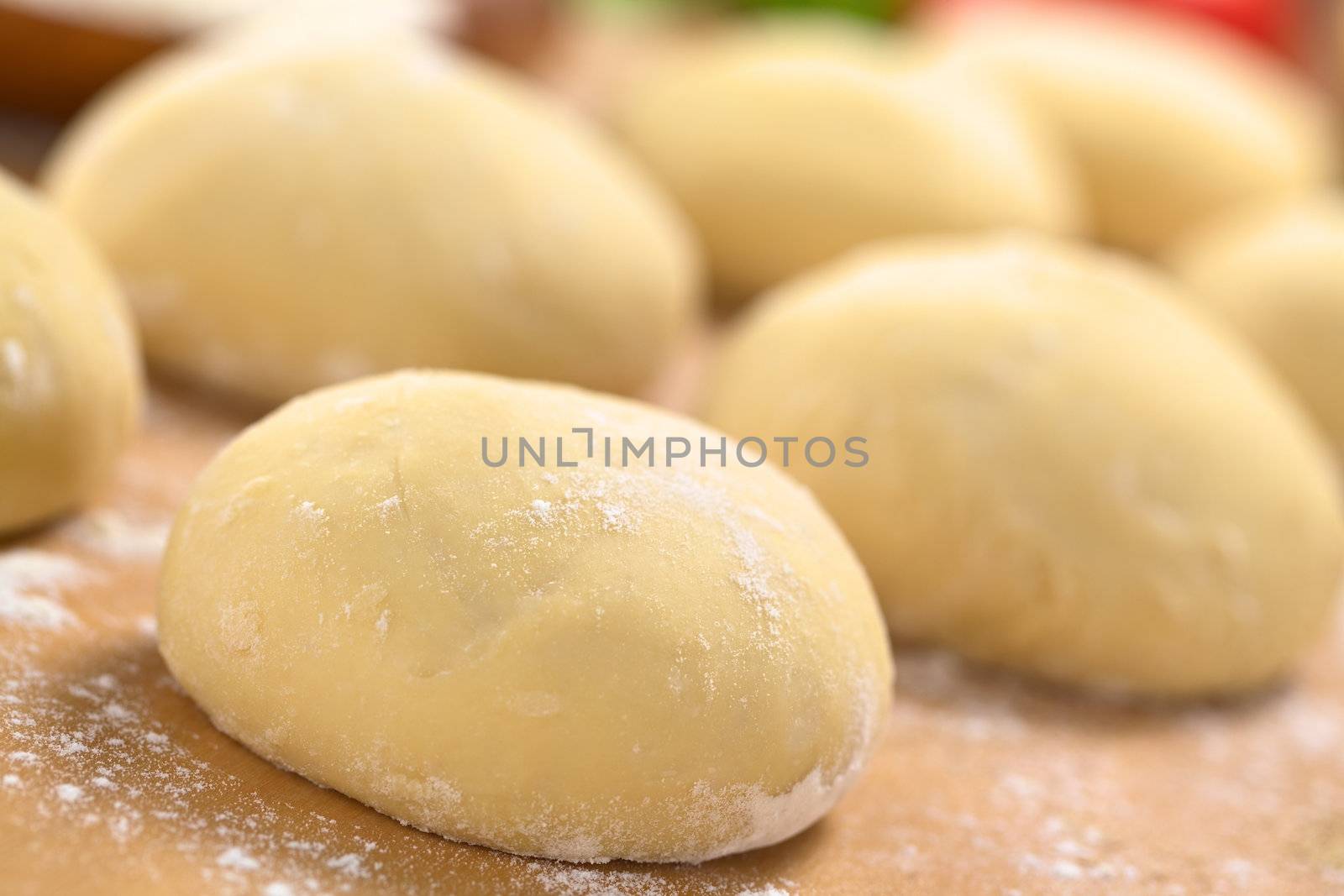 Small balls of fresh homemade pizza dough on floured wooden board (Selective Focus, Focus one third into the first pizza dough) 