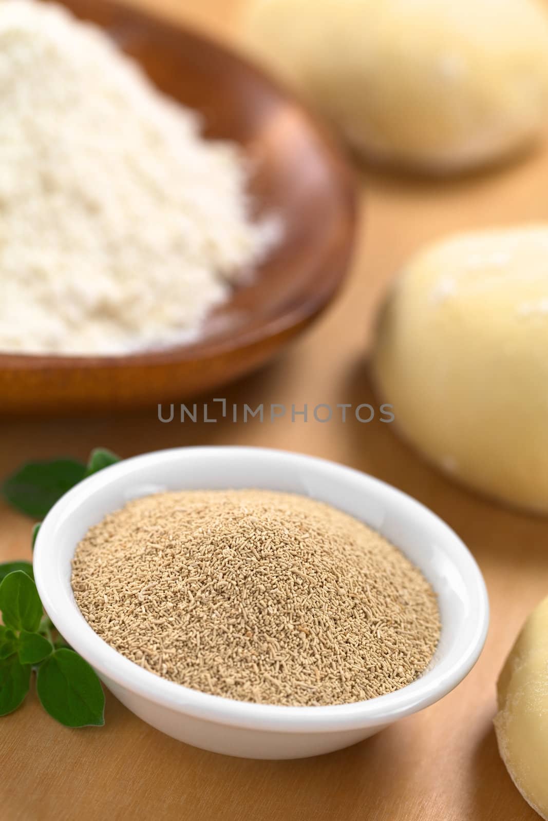 Active dry yeast in small bowl with fresh oregano, flour and dough (Selective Focus, Focus in the middle of the dry yeast)  