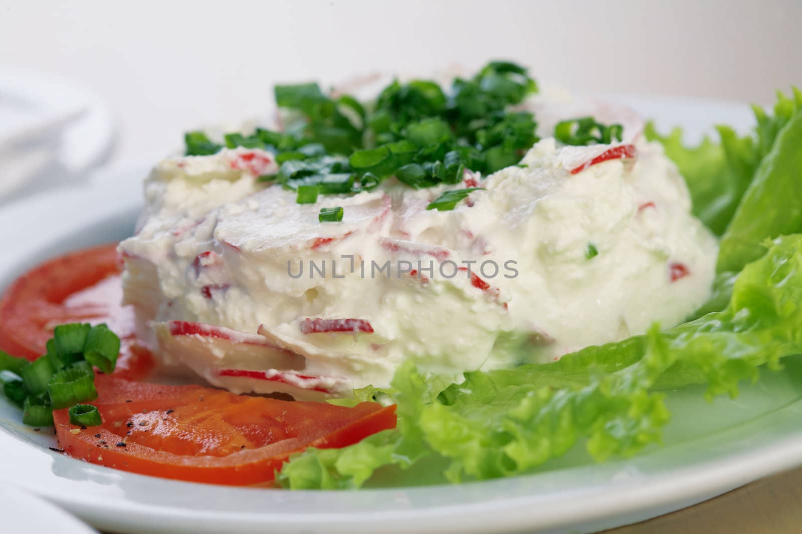 Close-up picture of a radish salad with lettuce, tomato, parsley and mayonnaise on the plate.