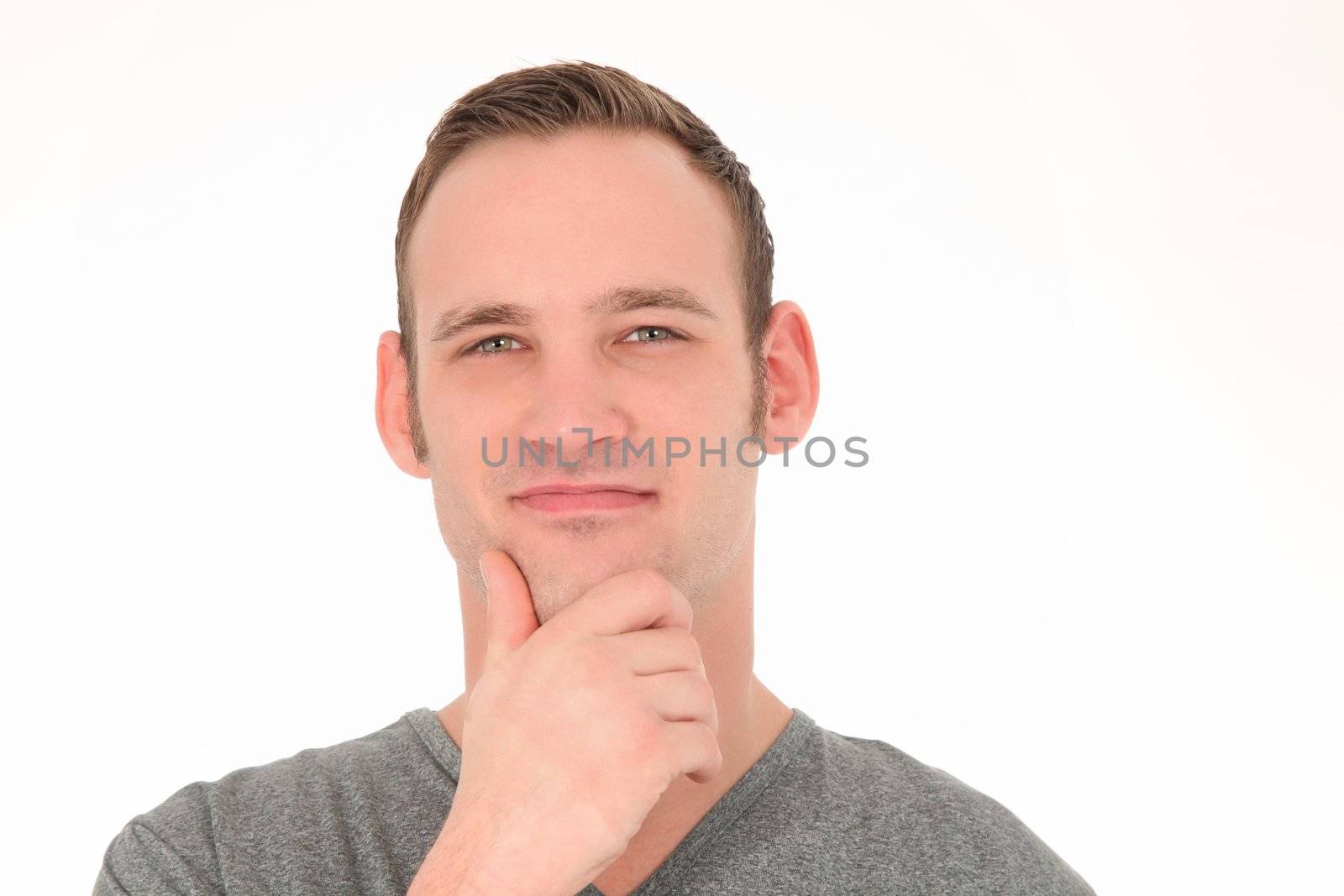 Happy thoughtful young man smiling as he stands with his hand to his chin isolated on white