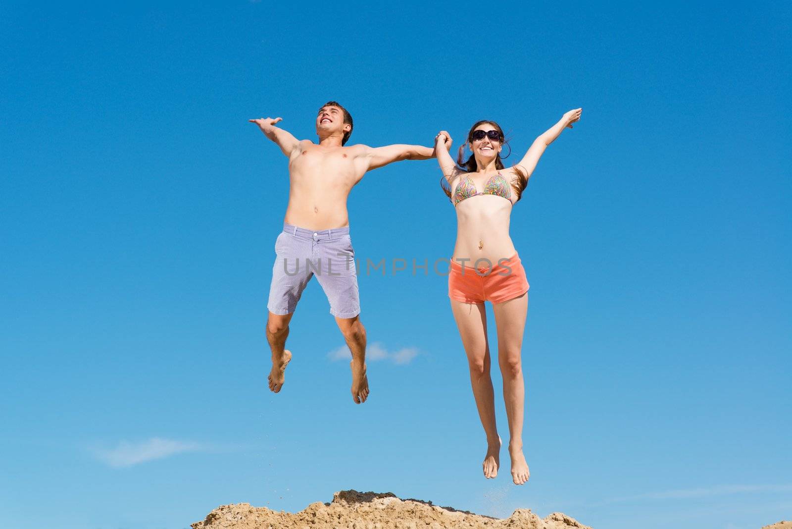 couple jumping together holding hands on a background of blue sky