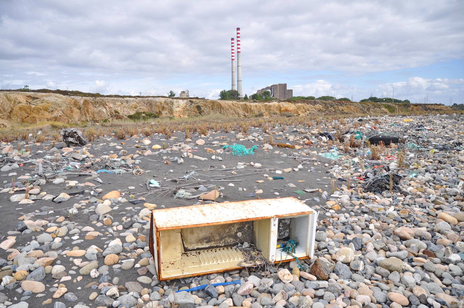 Trashed fridge on the seashore next to a factory