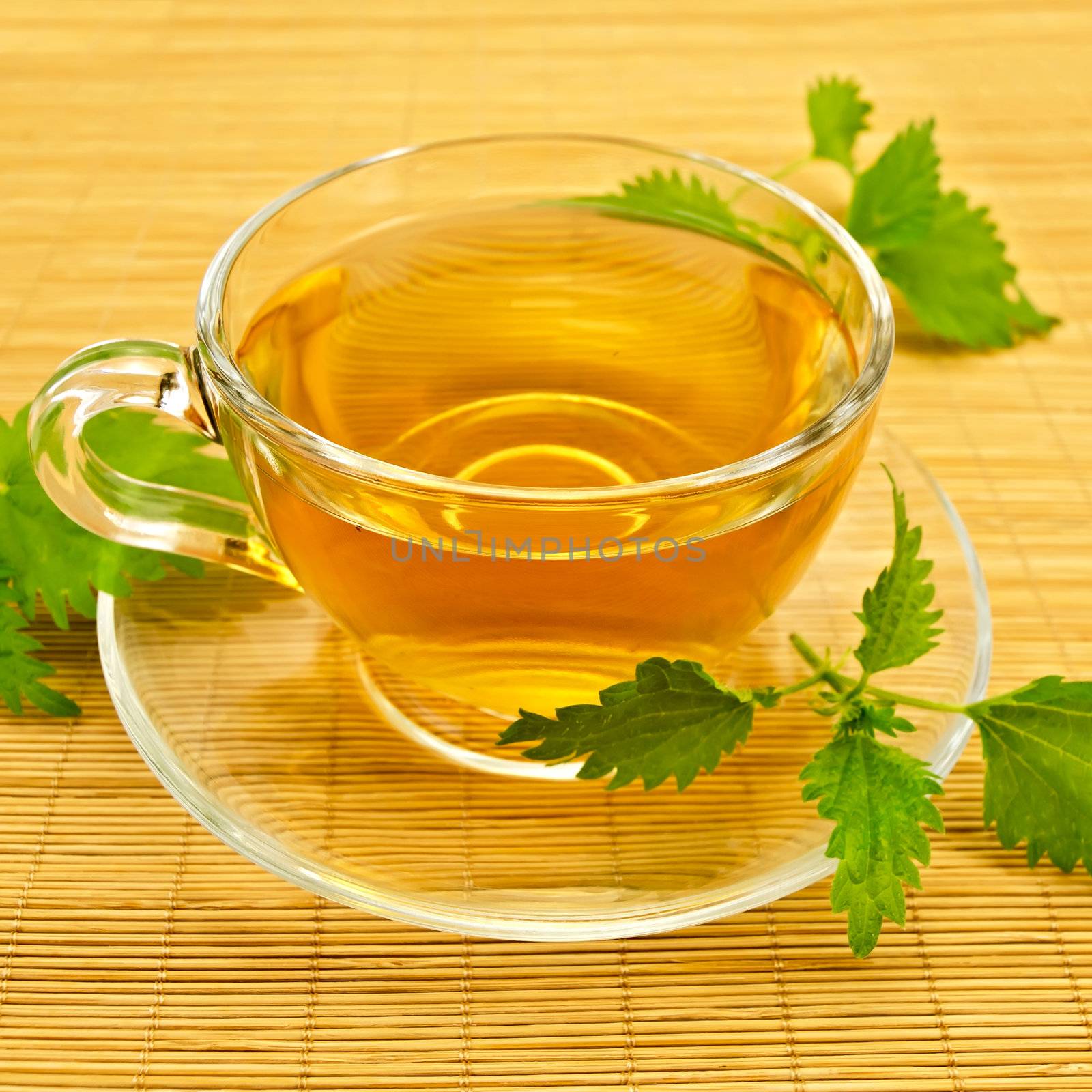 Herbal tea in a glass cup and saucer, three twig nettle on a bamboo napkin