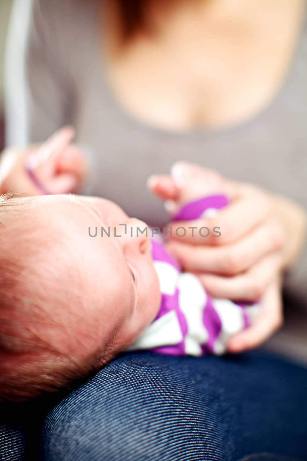 Young mother playing with her tiny baby holding its hands as it lies on her lap
